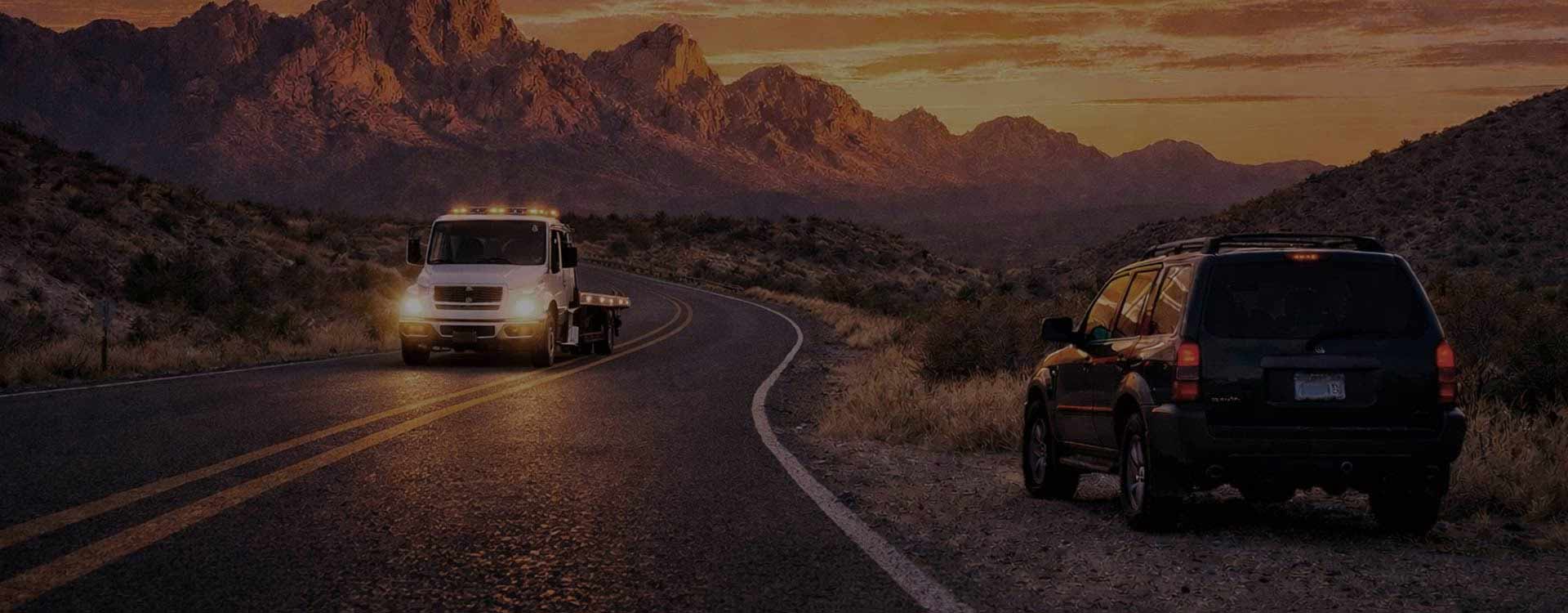 Flatbed tow truck responding to a stranded SUV on a mountain road near Big Bend National Park at sunset.